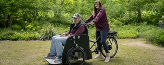 Haus St. Raphael Ein Bewohner fährt gemeinsam mit einer Mitarbeiterin auf einem Rollstuhlfahrrad durch die Natur.