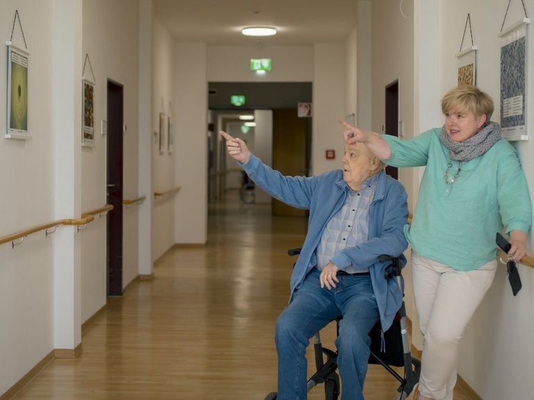 Ein Bewohner betrachtet gemeinsam mit der Quartiersmanagerin seine eigens gefertigten Kunstwerke, die an der Wand hängen.