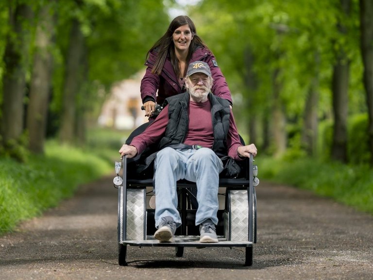 Eine Mitarbeiterin fährt gemeinsam mit einem Bewohner auf einem Rollstuhlfahrrad durch die Natur.